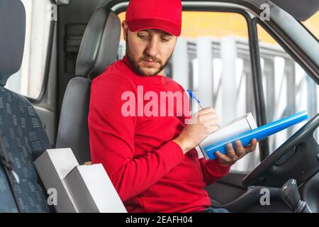 Der Lieferer registriert die Details des Produkts während des Sitzens Auf dem Fahrersitz in einem Fahrzeug Stockfoto