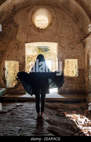 Rückansicht der Frau im schwarzen Umhang in alten verlassen Kapelle Stockfoto