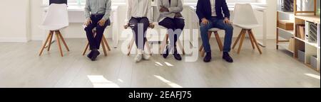 Zugeschnittenes Bild der Beine von verschiedenen Menschen sitzen auf Stühlen und warten an der Reihe. Stockfoto