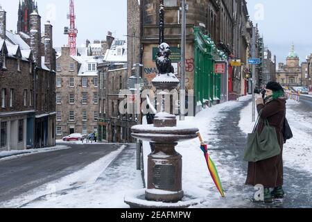 Eine Frau, die ein Bild von der Statue der Greyfriars Bobby im Stadtzentrum von Edinburgh mit Schnee bedeckt Stockfoto