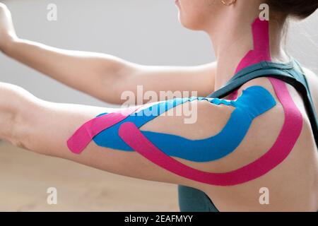 Nahaufnahme einer jungen frauenpassenden Schulter mit elastischem therapeutischem Kinetic Tape auf ihrer Schulter. Durchführung von Übungen zu Hause. Kinesiologie Physikalische Therap Stockfoto