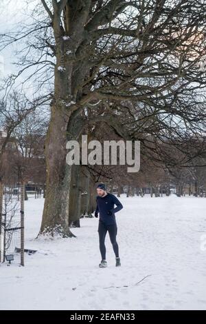 Ein Mann, der in einem von Schnee bedeckten Park läuft Die frühen Morgenstunden Stockfoto