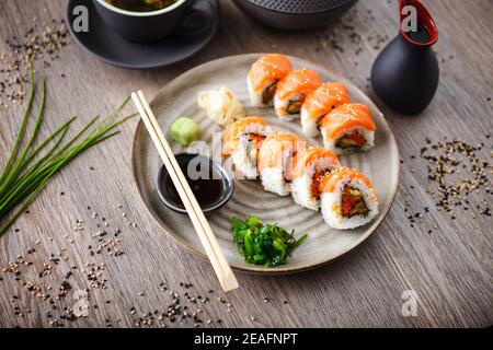 Sushi-Maki-Brötchen mit Lachs, Avocado, fliegendem Fischrogen und Gurke auf einem Teller mit Essstäbchen, Sojasauce, Wasabi und Ingwer. Traditionell japanisch Stockfoto
