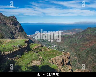 Blick auf Klippen und felsige atlantikküste im Nordwesten von Gran Canaria mit Blick auf die Stadt Agaete, Serpentinenstraße und grüne Hügel. Kanarische Inseln Stockfoto