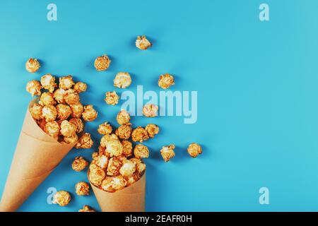 Karamell Popcorn in einem Papierumschlag auf blauem Hintergrund. Köstliches Lob für das Ansehen von Filmen, Serien, Cartoon. Freier Speicherplatz, Nahaufnahme. Minimalis Stockfoto