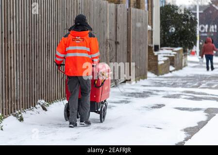 Royal Mail Postarbeiter schiebt einen Postwagen in Southend on Sea, Essex, Großbritannien, mit Schnee von Storm Darcy. Eisige Straßenverhältnisse. Weitermachen Stockfoto