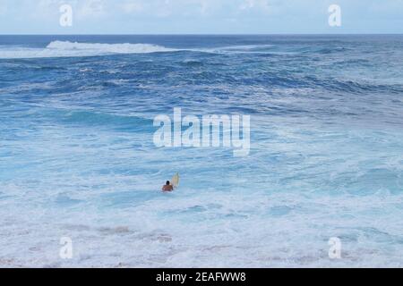 Surfer Mann schwimmt mit einem Brett, um die Wellen zu treffen Im Meer Stockfoto