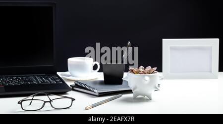 Weißer Tisch mit Laptop. Büro-Homeworkspace für Arbeit oder Studium in Office Interior. Schwarzer Laptop mit leerer Display-Layout-Vorlage auf Schwarz Stockfoto