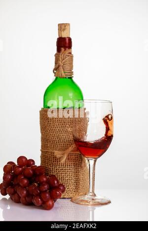 Rotwein im Glas mit Trauben und Flasche auf weißem Hintergrund. Stockfoto