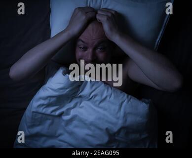 Mann liegt im Bett, gestresst, besorgt und kann nicht schlafen und starrt an die Decke. Stockfoto