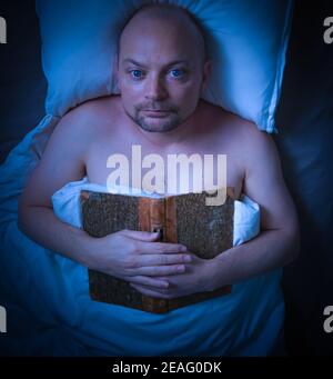 Mann, der im Bett lag und ein Buch sah nachdenklich aus. Stockfoto