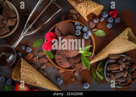 Dunkles Schokoladeneis. Viel Schokoladeneis mit Schokoladenbohnen, Puder und Stücken, mit Eiscreme-Waffelzapfen und sommerfrischen Beeren Stockfoto