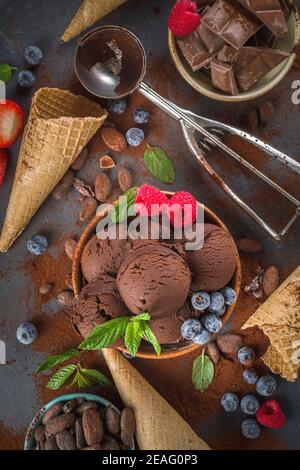 Dunkles Schokoladeneis. Viel Schokoladeneis mit Schokoladenbohnen, Puder und Stücken, mit Eiscreme-Waffelzapfen und sommerfrischen Beeren Stockfoto