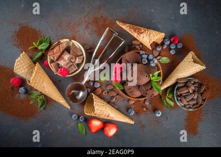Dunkles Schokoladeneis. Viel Schokoladeneis mit Schokoladenbohnen, Puder und Stücken, mit Eiscreme-Waffelzapfen und sommerfrischen Beeren Stockfoto