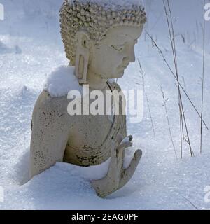 Eine cremeweiße buddha-Statue im Winter in einem deutschen Garten. Der buddha ist tief im Schnee versunken. Seine Handbewegung ist noch sichtbar. Stockfoto