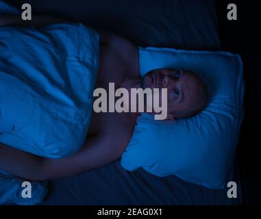 Der Mann, der im Bett liegt, kann nicht schlafen und starrt an die Decke. Stockfoto