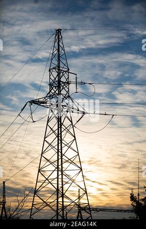 Ein Strommast auf der Basis eines Trassens gegen den Himmel und Wolken bei Sonnenuntergang gebaut. Stockfoto