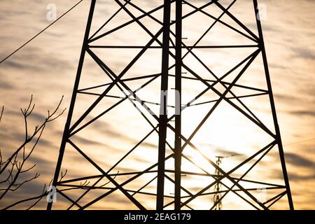 Ein Strommast auf der Basis eines Trassens gegen den Himmel und Wolken bei Sonnenuntergang gebaut. Stockfoto