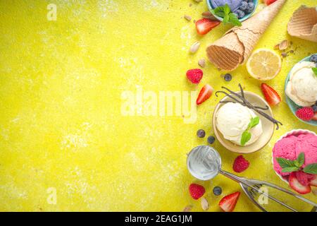 Verschiedene bunte Eisbällchen in verschiedenen Schüsseln, mit Eiswaffeln Zapfen und Geschmackszutaten - Pistazien, Beeren, Zitrone, Schokolade, Stockfoto