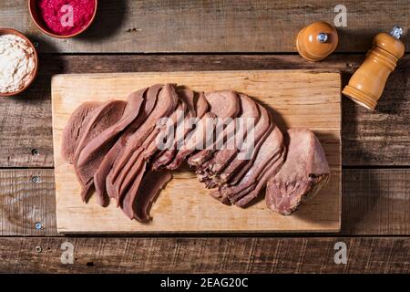 Gebackene Rinderzunge in Scheiben geschnitten, serviert mit Meerrettich-Sauce rot und weiß und Fleischmesser auf Holzschneidebrett auf Holz Hintergrund. Draufsicht. Stockfoto