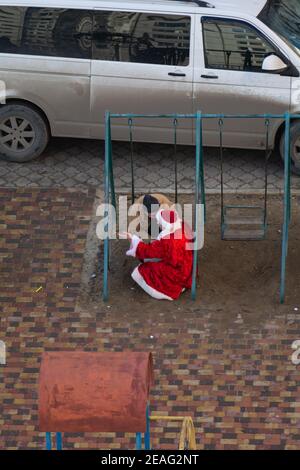 Tiraspol, Moldawien - 1. Januar 2021: Ein betrunkener Mann sitzt auf einer Kinderschaukel und hat einen Dialog mit einem betrunkenen Mann in einem Weihnachtsmann-Kostüm Stockfoto