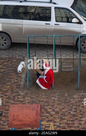 Tiraspol, Moldawien - 1. Januar 2021: Ein betrunkener Mann sitzt auf einer Kinderschaukel und hat einen Dialog mit einem betrunkenen Mann in einem Weihnachtsmann-Kostüm Stockfoto