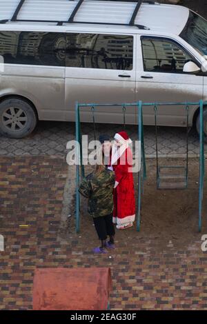 Tiraspol, Moldawien - 1. Januar 2021: Ein betrunkener Mann sitzt auf einer Kinderschaukel und hat einen Dialog mit einem betrunkenen Mann in einem Weihnachtsmann-Kostüm Stockfoto