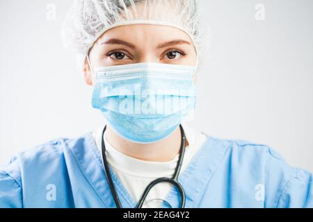 Betroffen kaukasischen UK NHS Arzt isoliert auf weißem Hintergrund Porträt, tragen Medizinische PSA Persönliche Schutzausrüstung, Gesichtsmaske und Haarschutz Stockfoto