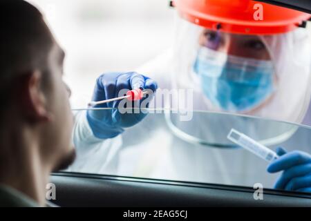 COVID-19 Drive-Thru-Patientenprobe, medizinische Mitarbeiterin, die Nasenabstrich durchführt Auf jungen Mann durch Fahrzeugfenster, Coronavirus Punkt c Stockfoto