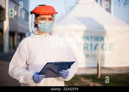 Besorgt erschöpft und gestresst Frontline UK NHS Arzt, trägt PSA & Gesichtsschutz, außerhalb des Krankenhauses Patienten Triage Zelt Quarantäne, spezielle US COVID-19 Zoll Stockfoto