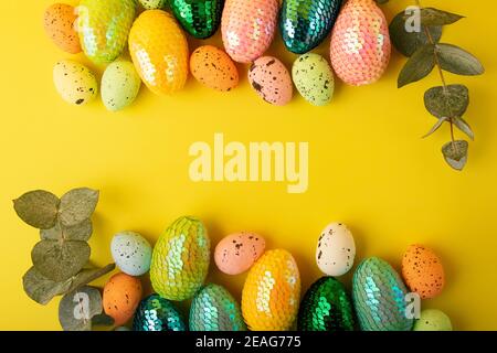 Rahmen aus bunten ostereiern.Frische Eukalyptus Zweig in der Nähe.trendy gelben Hintergrund.Kreatives Layout mit Kopierraum. Stockfoto