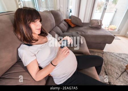 Schwangere Frau auf einer Couch, die ihren Blutzucker testet Gestationsdiabetes mit gutem Ergebnis Stockfoto