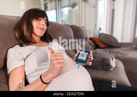 Schwangere Frau auf einer Couch, die ihren Blutzucker testet Gestationsdiabetes mit gutem Ergebnis Stockfoto