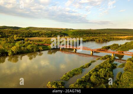Luftaufnahme einer schmalen Straßenbrücke, die sich über einen schlammigen, breiten Fluss in grüner ländlicher Umgebung erstreckt. Stockfoto