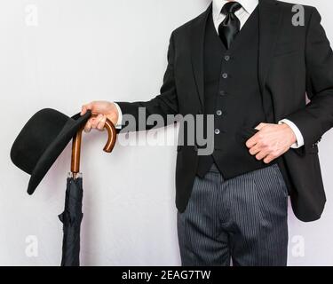 Portrait of man in Dark Suit Halten Bowler Hut und Regenschirm auf weißem Hintergrund. Klassischer und exzentrischer englischer Gentleman. Britischer Geschäftsmann. Stockfoto