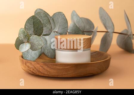 Hautpflege-Verpackung mit Creme Aufenthalt in der Holzplatte.Eucalyptus Zweig hinter.Pastel isometrischen Hintergrund, organisches Konzept. Stockfoto