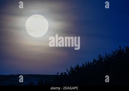 Der Vollmond steigt hinter dem Berg auf Stockfoto