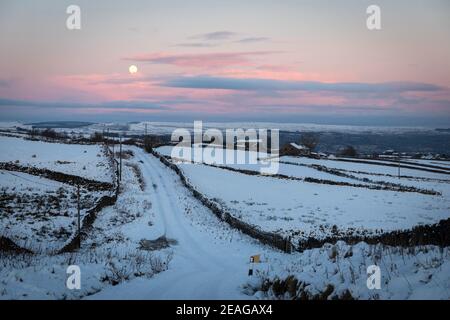 Ein Vollmond steigt über Newsholme auf, während der Winter die Landschaft ergreift. Stockfoto