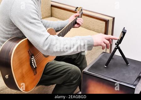 Der Musiker komponiert ein Lied auf der Gitarre und nimmt es auf seinem Handy auf. Stockfoto