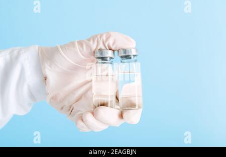 Covid 19-Impfstoff in Flaschen aus Glasfläschchen, Medikamentenflüssigkeit in der Hand des Arztes. Impfungen als Behandlung auf blauem Hintergrund. Covid 19 Gesundheitswesen Stockfoto