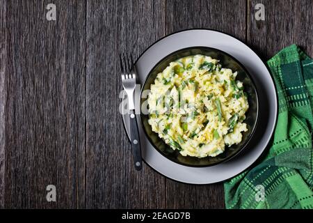Traditionelle irische Colcannon aus Kartoffelpüree, Grünkohl, Knoblauch, geschmolzener Butter und Frühlingszwiebeln auf einem schwarzen Teller mit Besteck auf einem dunklen Holzbackg serviert Stockfoto