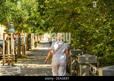 PRAG, TSCHECHISCHE REPUBLIK - JULI 2018: Person mit Sonnenhut zu Fuß entlang einer schattigen Allee im Prager Stadtzentrum. Stockfoto