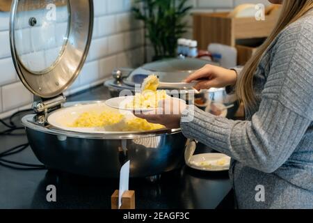 Keine Gesichtsfrau, die Rühreier in ein Selbstbedienungsbüffet mit warmem Frühstück im Hotel legte. Kontinentales Frühstückskonzept. Selektiver Fokus, Kopie sp Stockfoto