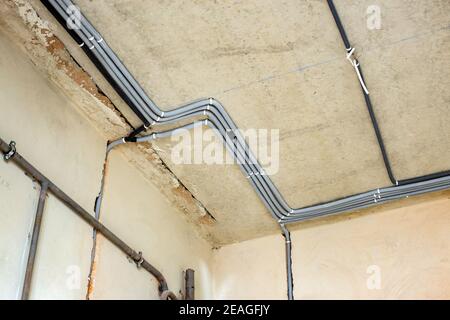 Elektrokabel in einer Schutzwellung an der Decke und an der Wand in einem Raum, in dem Bauarbeiten durchgeführt werden. Stockfoto