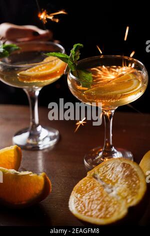 Feiern Sie Silvester 2022 mit Wunderkerzen Feuerwerk und trinken Cocktails. Minze mit Orangenscheibe in einem Cocktailglas gefüllt mit Alkoholcocktail Stockfoto