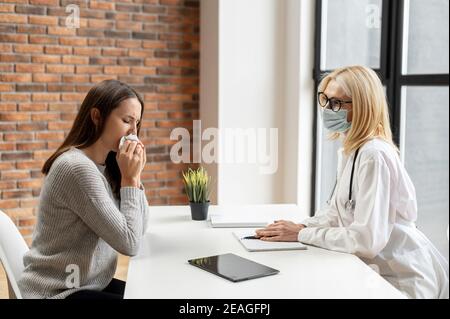 Reife weibliche blonde Arzt trägt eine Brille, Uniform, Stethoskop, und Schutzmaske Blick auf die medizinischen Testergebnisse, die Beratung zu einem Stockfoto