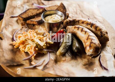 Gegrillte Würstchen mit Bier und Gemüse mit eingelegter Gurke, Kohlsalatsauce und Brot auf Pergament, Draufsicht. Stockfoto