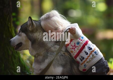 Glückliches kleines Mädchen mit ihrem Hund Husky. Happy Baby und Hund Umarmungen mit Zärtlichkeit lächelnd. Positive Emotionen von Kindern. Frohe Kindheit. Stockfoto