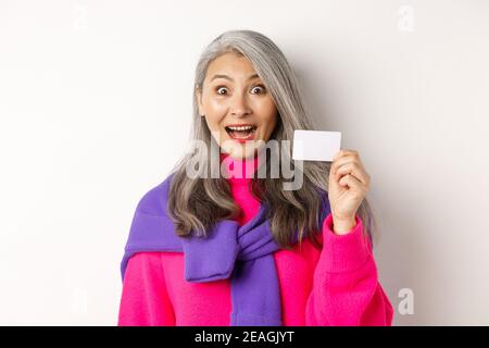 Einkaufskonzept. Glücklich asiatische alte aldy suchen beeindruckt und zeigt Kunststoff-Kreditkarte ihrer Bank, über weißem Hintergrund stehen Stockfoto