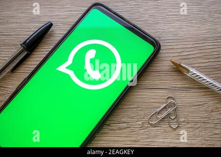 Smartphone mit grünem whatsapp-Logo auf Holztisch mit Stift-Büroklammern. Telefon-Datenschutz-Konzept mit Zuckerberg Social Media-Symbol. Stockfoto